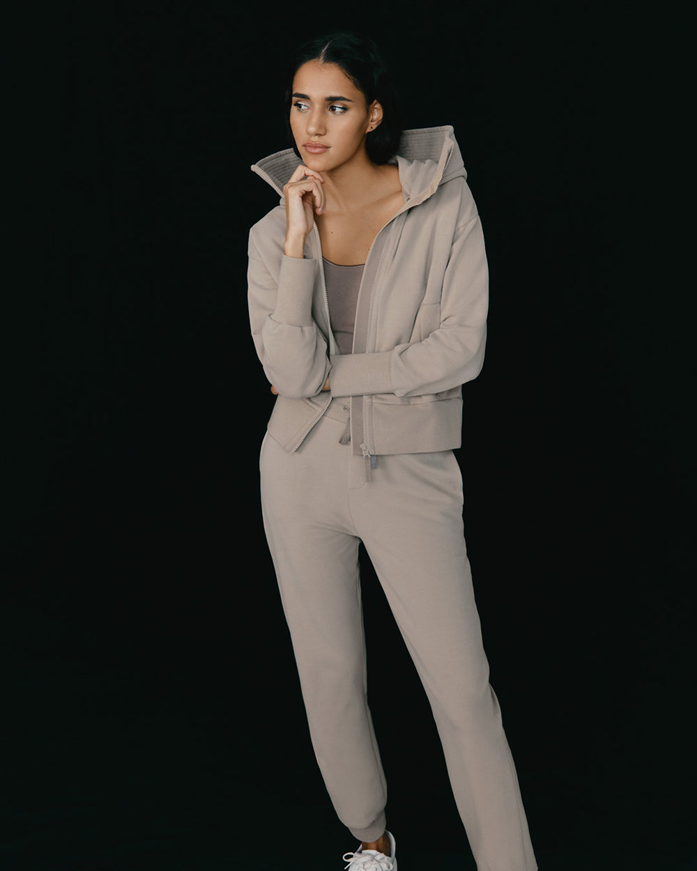 Woman in a tracksuit standing with hand on chin, looking to the side.