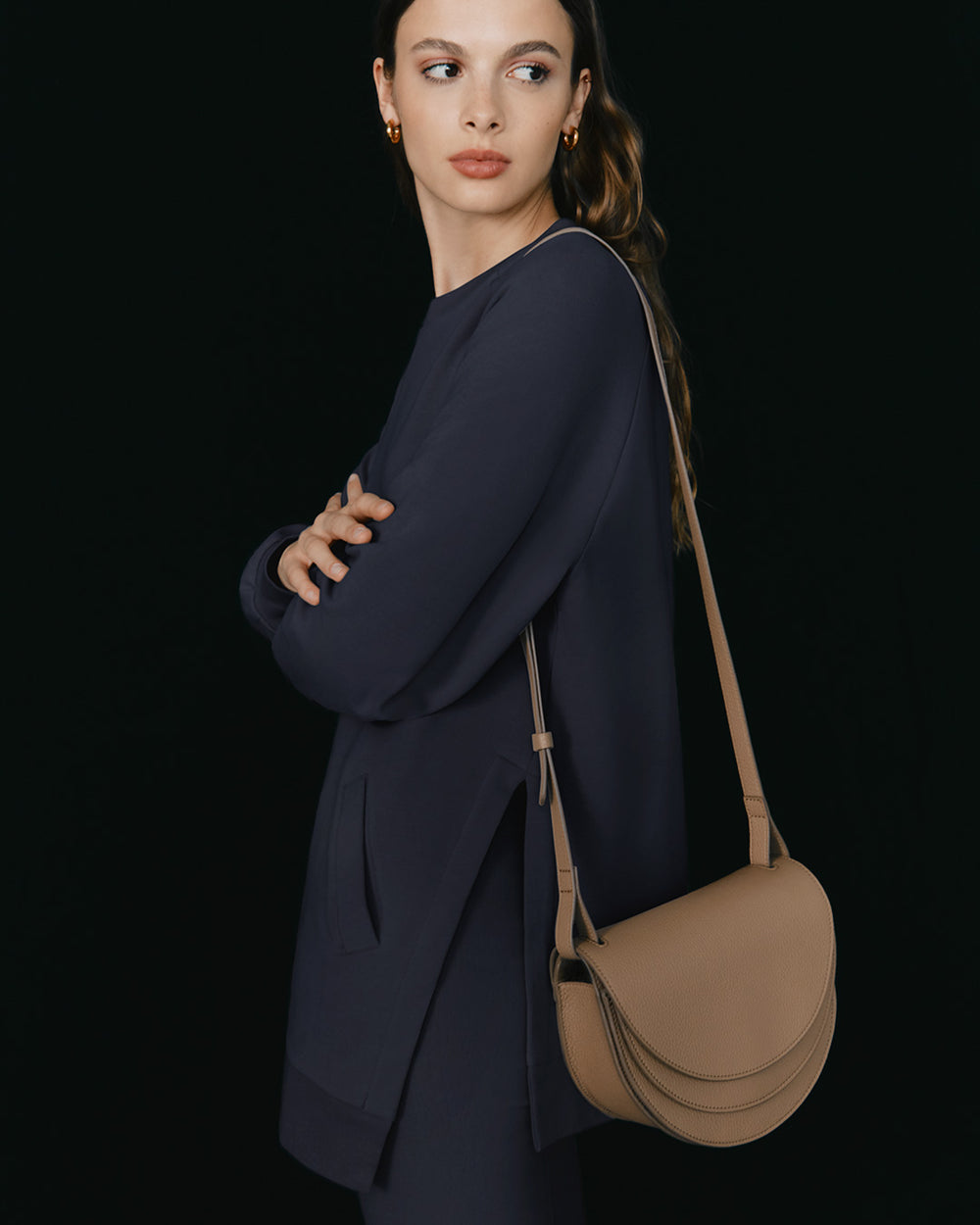 Woman standing with a shoulder bag, arms crossed.