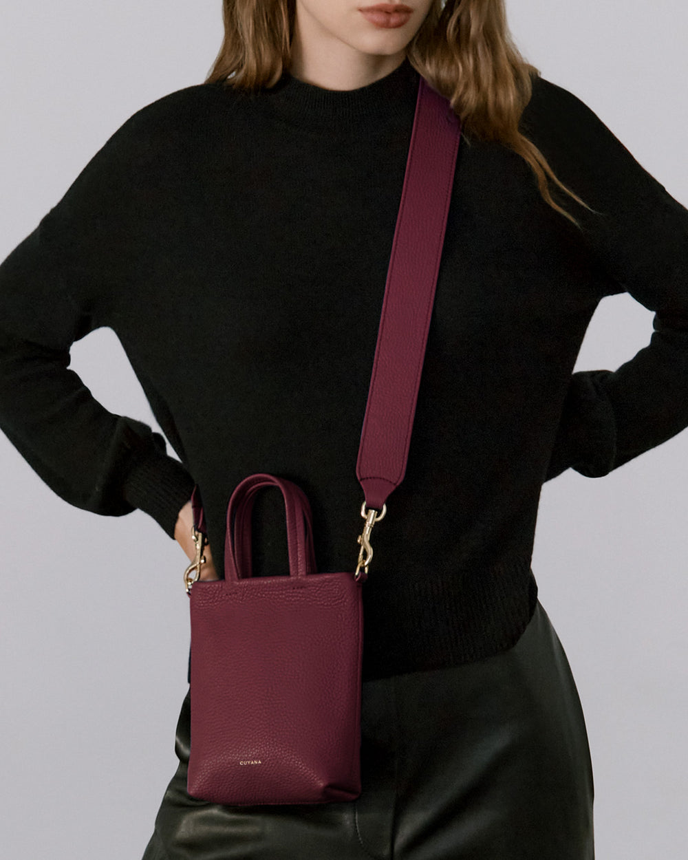 Person wearing a black top and holding a small crossbody bag with two handles.