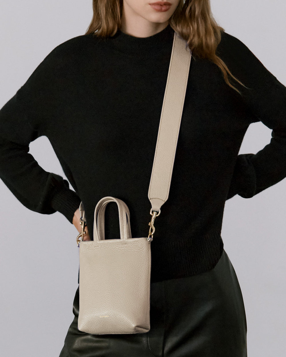 Person wearing a long-sleeved top and pants, holding a shoulder bag with both hands on their hips