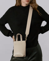 Person wearing a long-sleeved top and pants, holding a shoulder bag with both hands on their hips