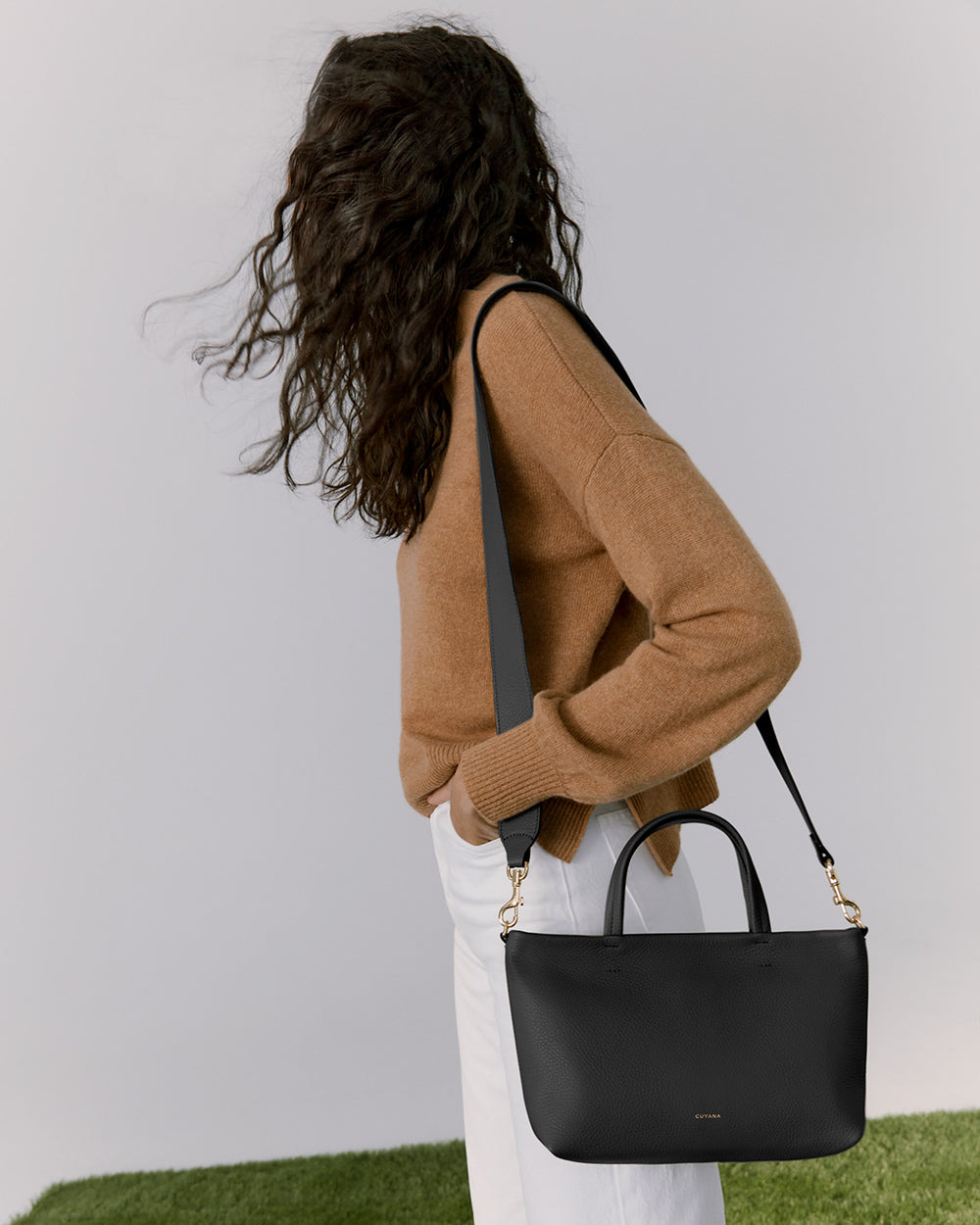 Woman from behind with curly hair carrying a handbag over her shoulder.