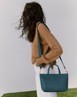 Person wearing a sweater with a shoulder bag and white pants, standing on grass