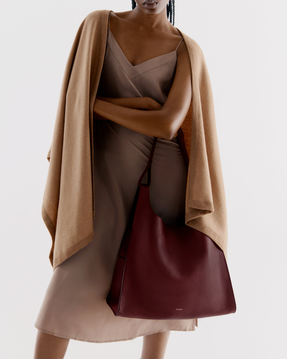 Person in a dress with a cape, holding a large shoulder bag.