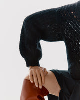 Person in a sweater leaning over with hand on their knee.