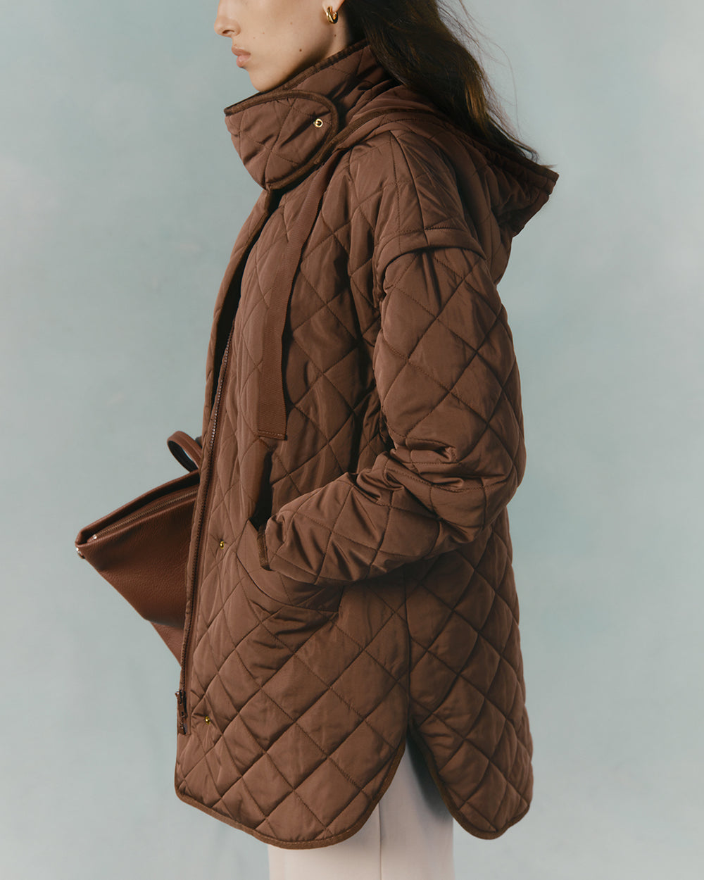 Side profile of a person wearing a quilted jacket and holding a clutch.