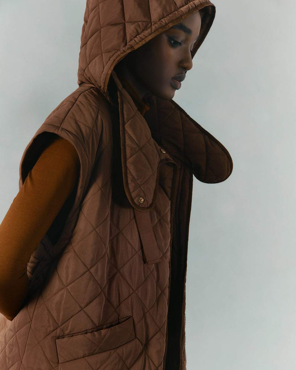 Person wearing a hooded vest looking downward.