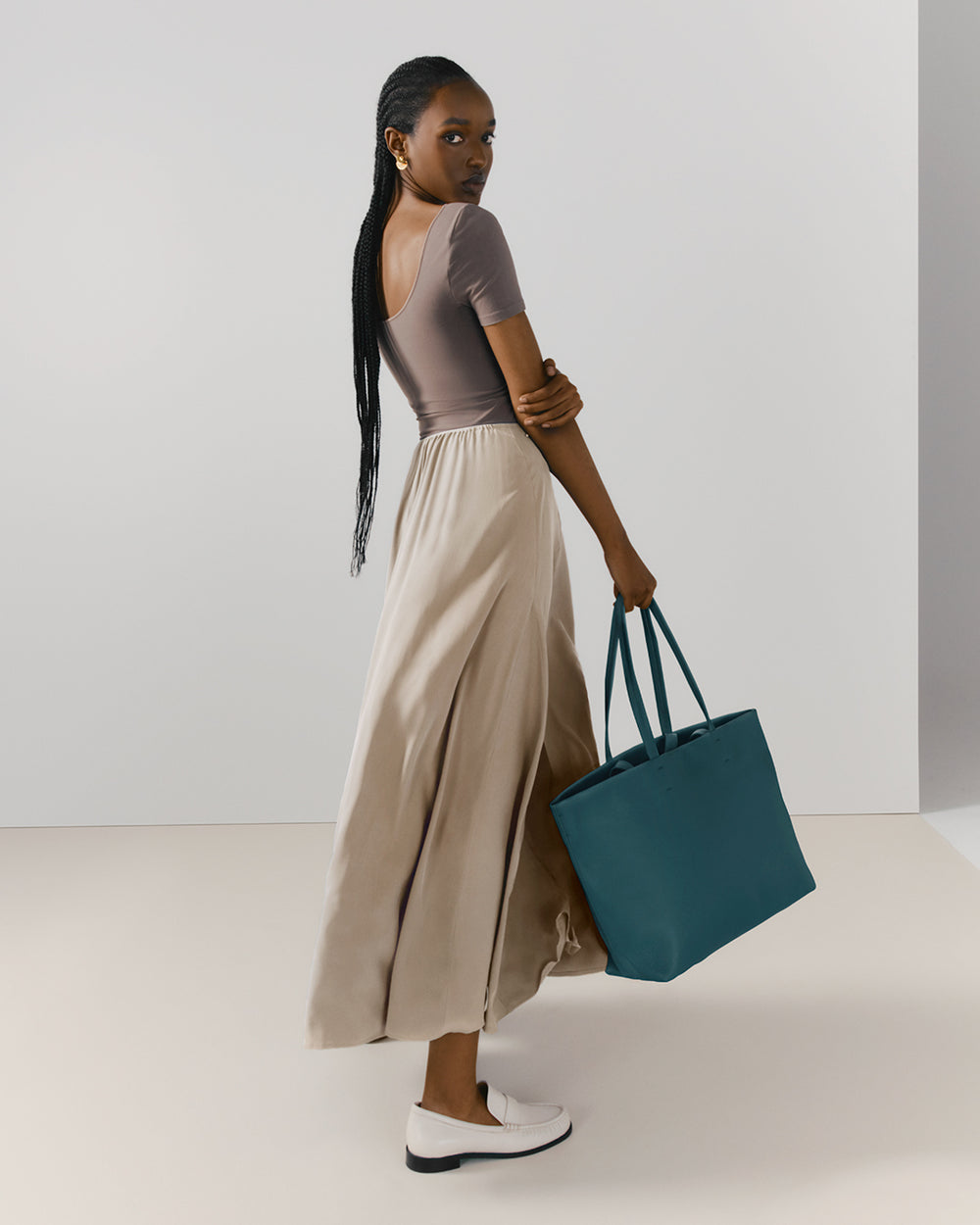 Person standing sideways wearing a long skirt and holding a large tote bag.