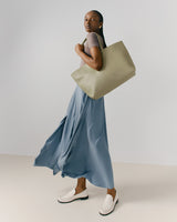 Woman standing with large bag over shoulder, looking over her shoulder.