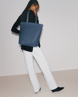 Person carrying tote bag, wearing long-sleeve top and pants.