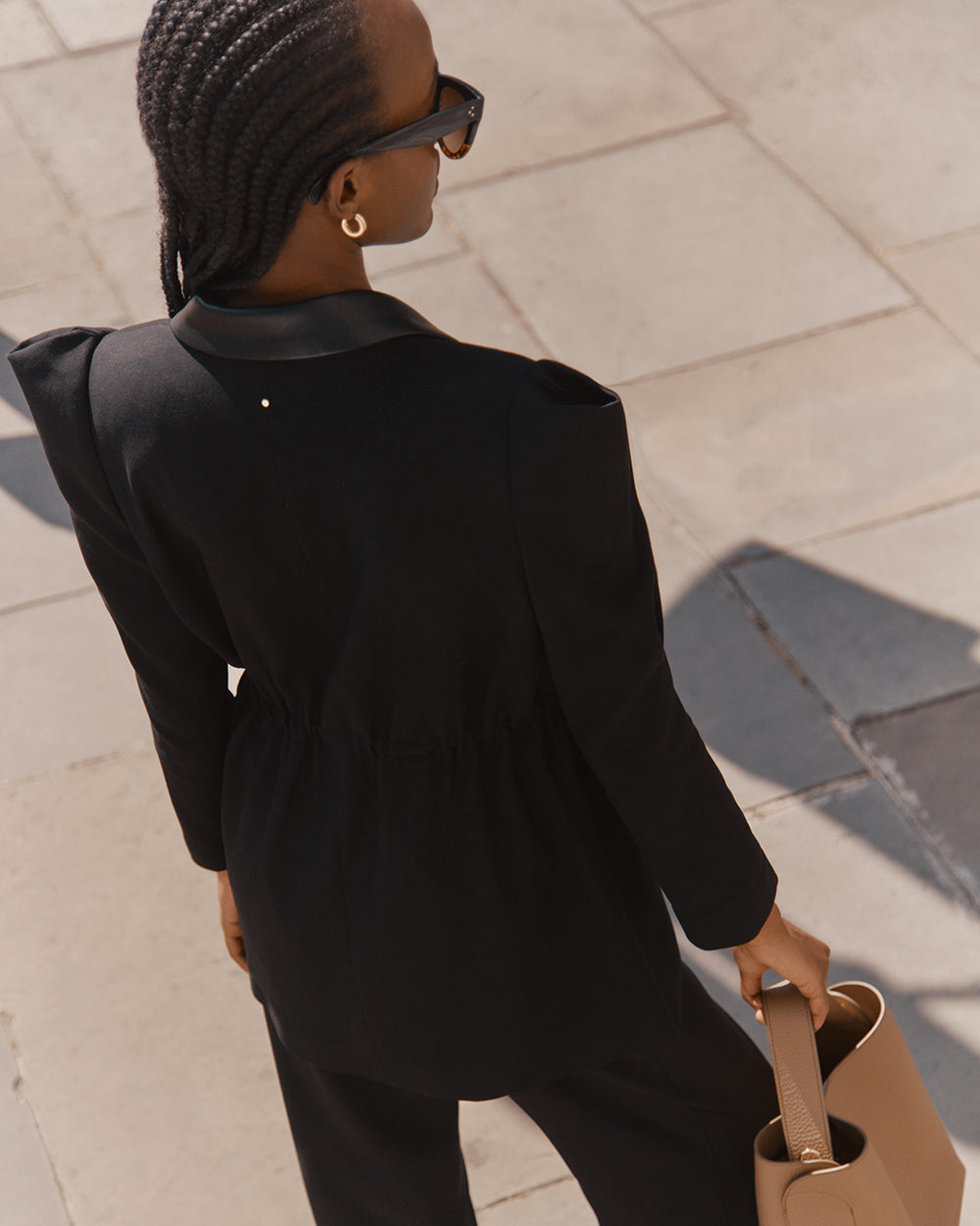 Woman in sunglasses holding a bag, walking on a street.