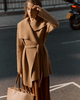 Woman standing on a sidewalk holding a bag and adjusting her hair