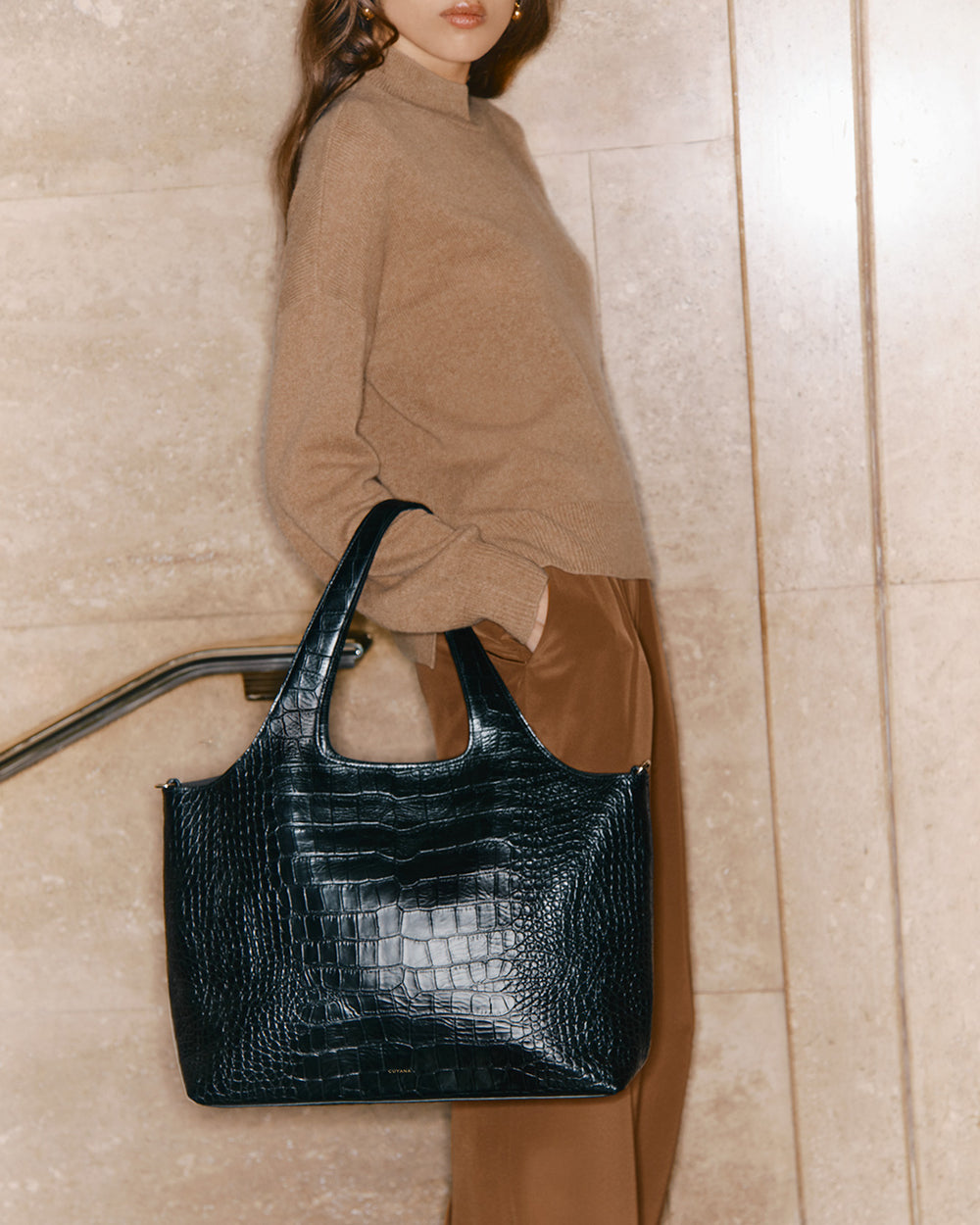 Woman in a turtleneck carrying a large handbag, standing indoors.