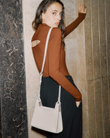 Woman with bag leaning against a wall, looking over her shoulder.
