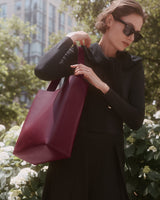 Person wearing sunglasses holds a large handbag while standing outside.