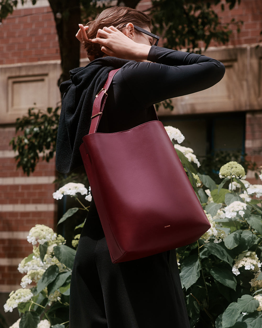 Person outside holding large leather shoulder bag near flowers and a building