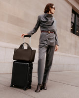 Person in a suit with a suitcase and a tote bag on the sidewalk