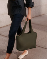 Person holding a tote bag while walking on a sidewalk