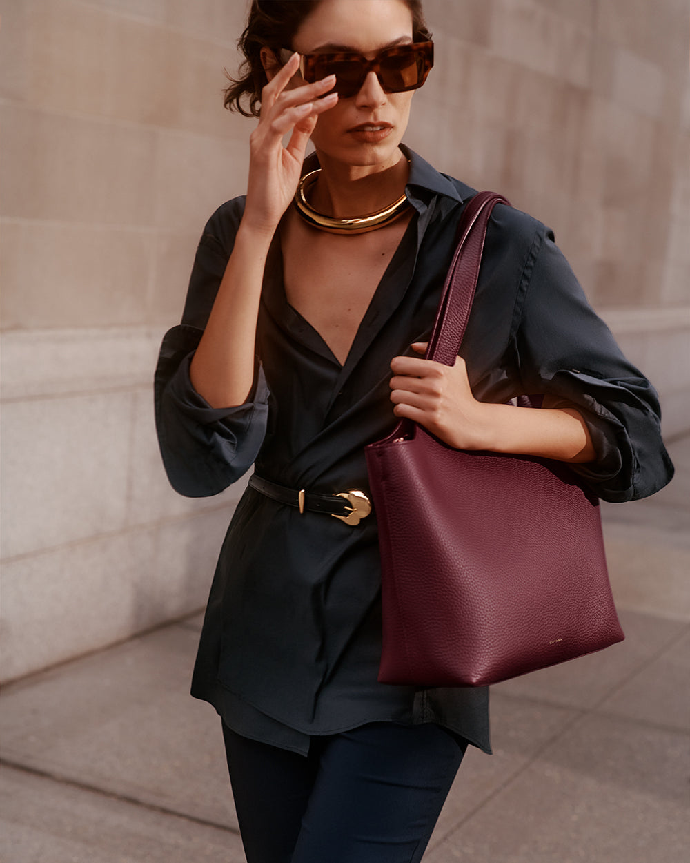 Person wearing sunglasses and holding a handbag while walking outdoors