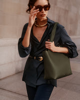 Person with sunglasses carrying a handbag and wearing a loose shirt with a belt.