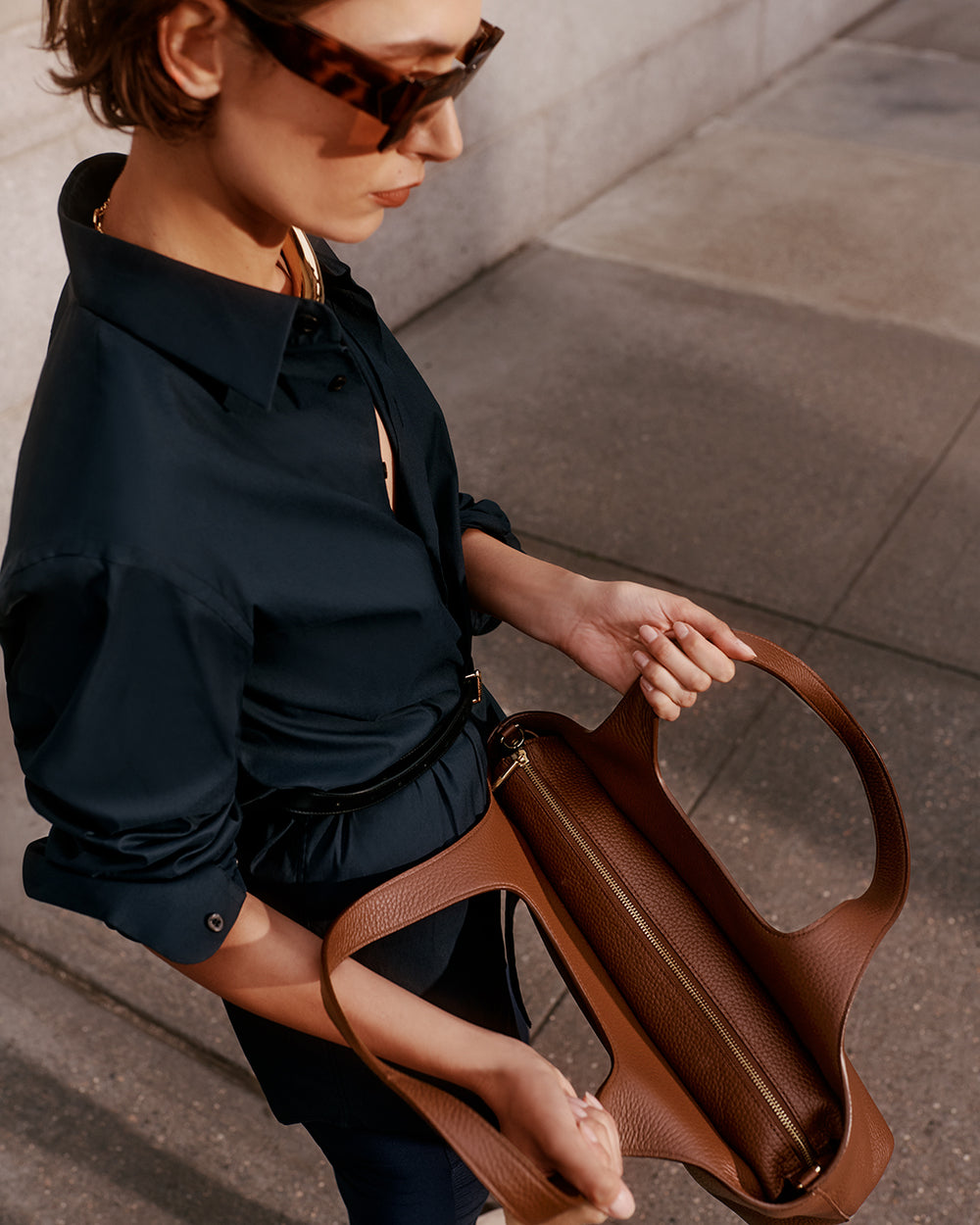 Person holding an open tote bag and wearing sunglasses.