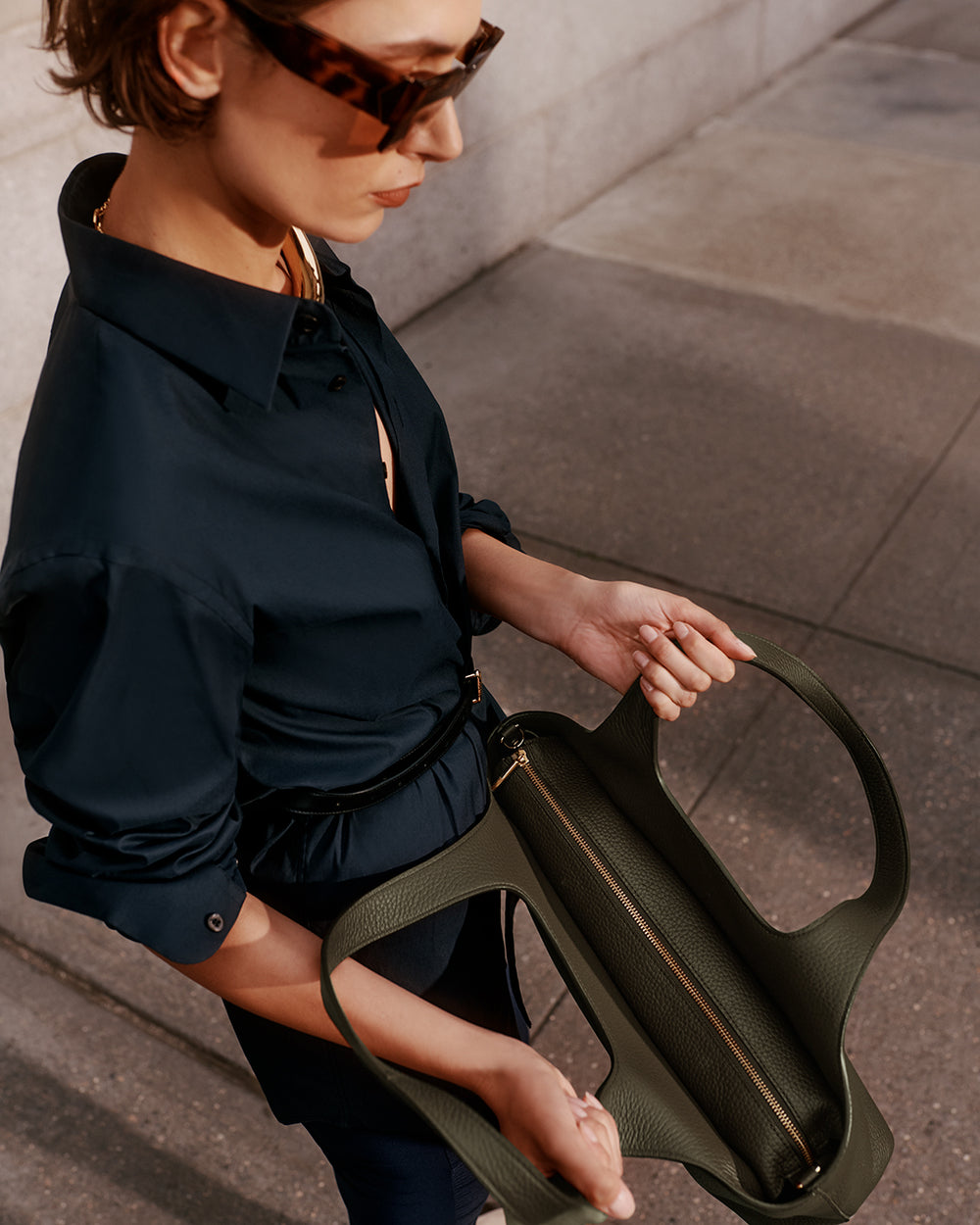 Person holding an open bag and looking down on the sidewalk