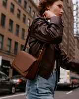 Person in a city street carrying a shoulder bag and wearing a jacket and jeans