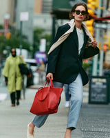 Person walking on a city street with red bag, wearing a blazer