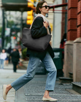 Person walking on street carrying a large bag and wearing sunglasses