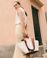 Woman holding a large tote bag stands by a building entrance.