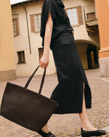 Person walking in street carrying a tote bag, wearing a long skirt and top