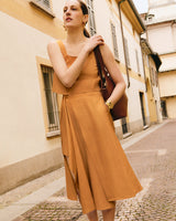 Woman in a sleeveless top and flowy skirt, walking on a cobblestone street carrying a bag.