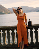 Woman in dress and sunglasses leans on railing by a lake with hills in background