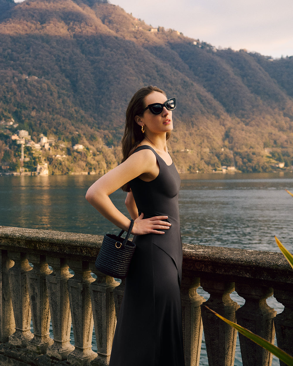 Woman in dress with a woven bucket bag by lake.