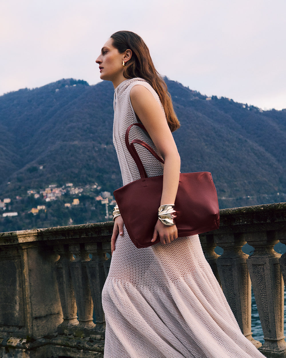 Person with shoulder bag walking on stone balcony with mountains in background.