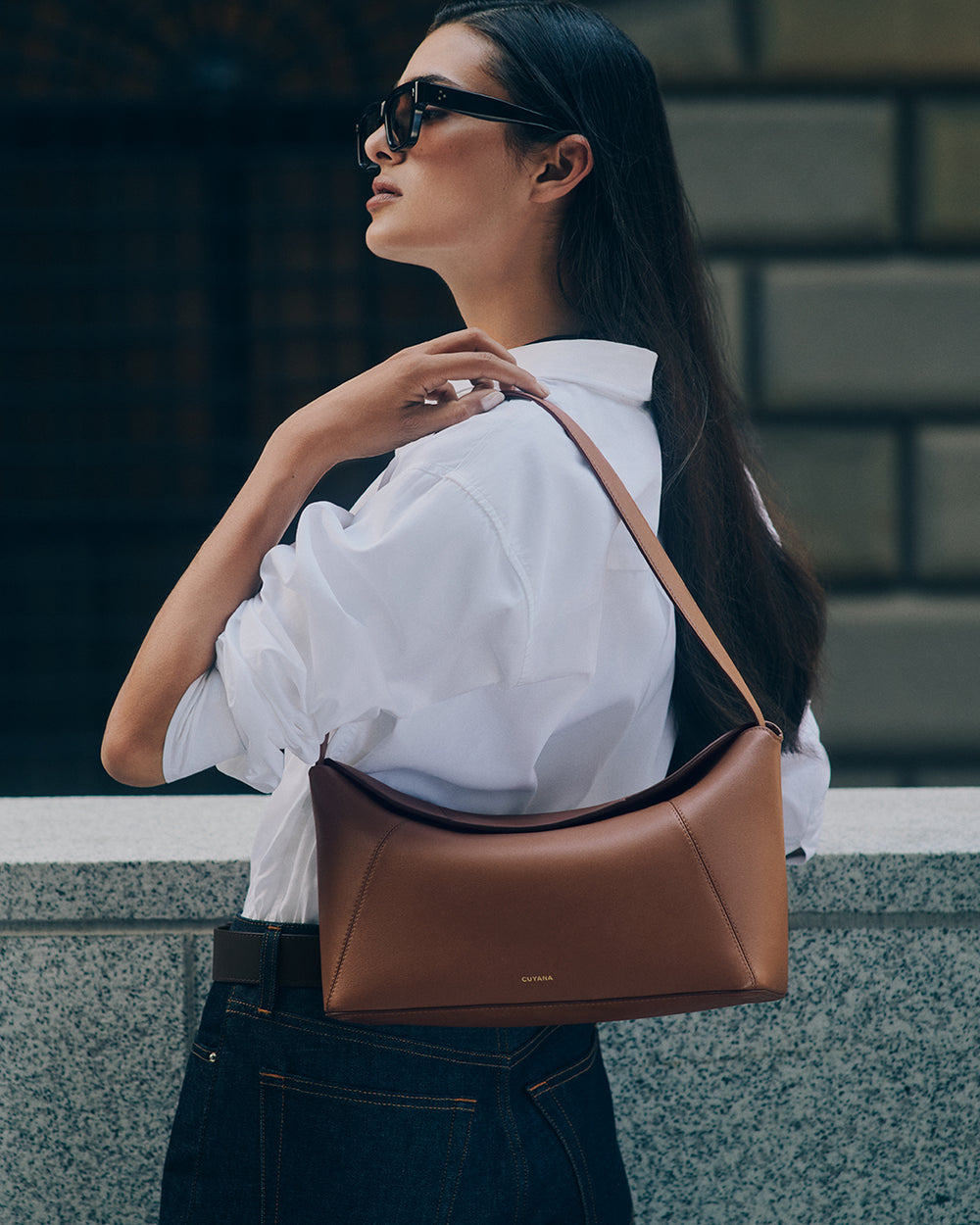 Person wearing sunglasses and carrying a shoulder bag.