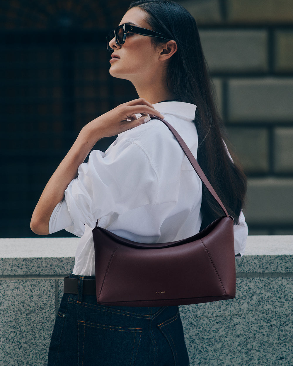 Person wearing sunglasses, white shirt, and jeans, holding shoulder bag.