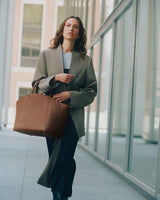 Person walking holding a large bag in front of a building with glass windows.
