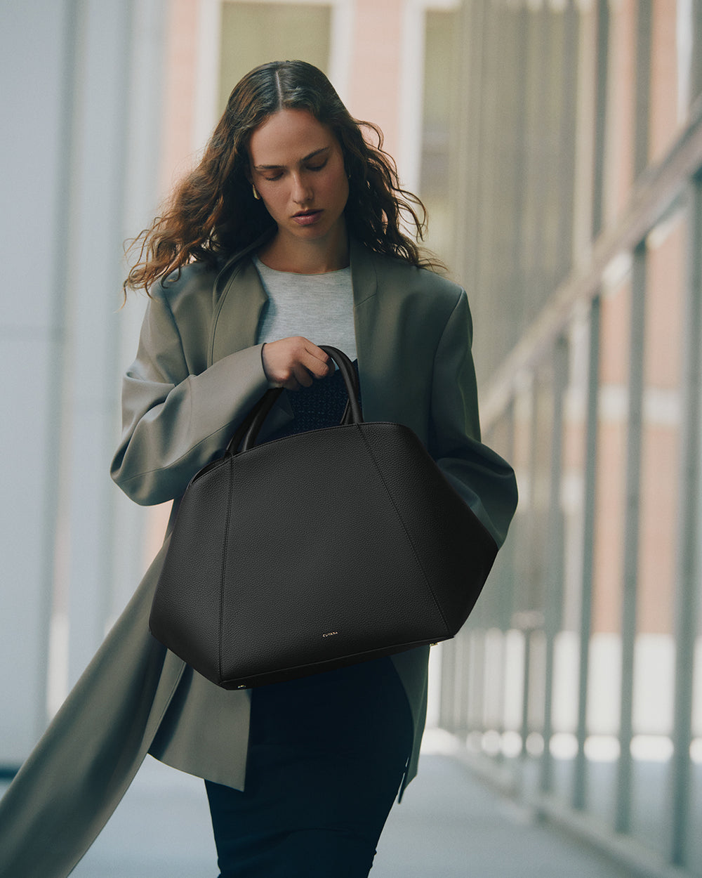 Person walking holding a handbag and wearing a long coat indoors