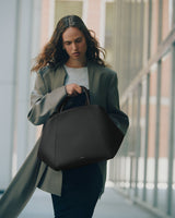 Person walking holding a handbag and wearing a long coat indoors