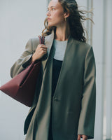 Person in jacket holding a large handbag while glancing to the side.