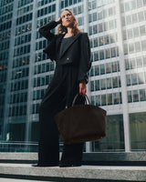 Person in suit standing on steps holding a large bag, skyscrapers in background.