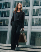 Person in suit holding a large handbag, standing on steps near tall buildings.
