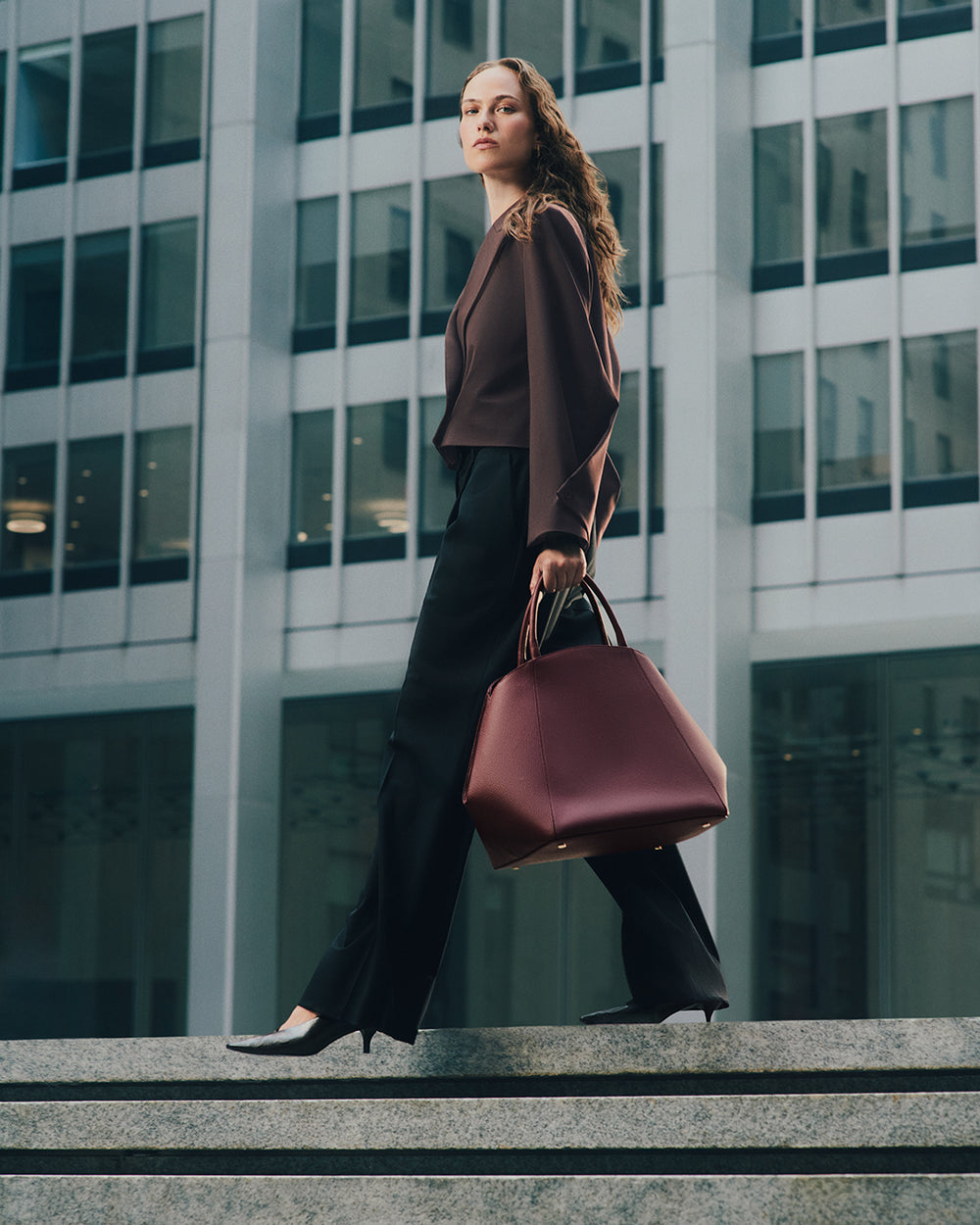 Person walking on steps carrying handbag in front of tall building