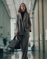 Person in suit holds a handbag walking in a corridor with large windows.