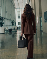 Person in a suit walking in a modern building, carrying a large handbag.