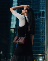 Woman in a cityscape standing with a purse over her shoulder.