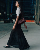 Person walking on a city sidewalk, holding a small handbag, wearing a long dress.