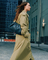 Person walking on city street wearing a long coat and carrying a handbag with a gold chain strap.
