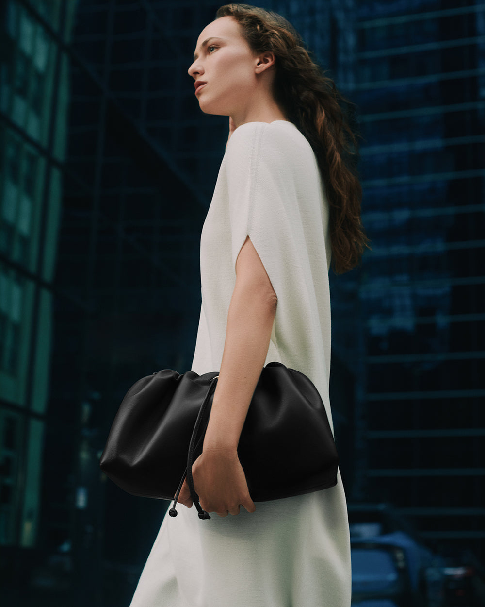 Person in a dress holding a gathered bag, standing outdoors near tall buildings.